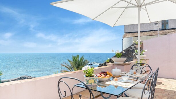 A table set with a fruit bowl, teapot, and cups, overlooking a coastal view. - Holiday Home in Santa Tecla Near Etna Beach (Acireale)