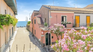 A narrow street with buildings on either side, a clear sky, and a view of the sea in the distance. - Holiday Home in Santa Tecla Near Etna Beach (Acireale)