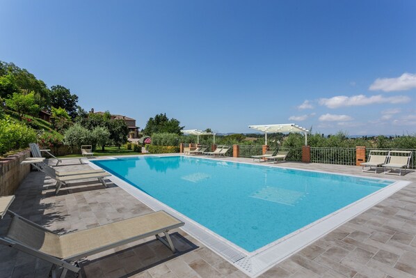 Una piscina rettangolare con bordo piastrellato, circondata da lettini e un pergolato.