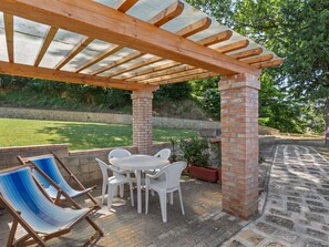 Una veranda coperta con un pilastro in mattoni, un tavolo con sedie e una poltrona reclinabile a righe blu.