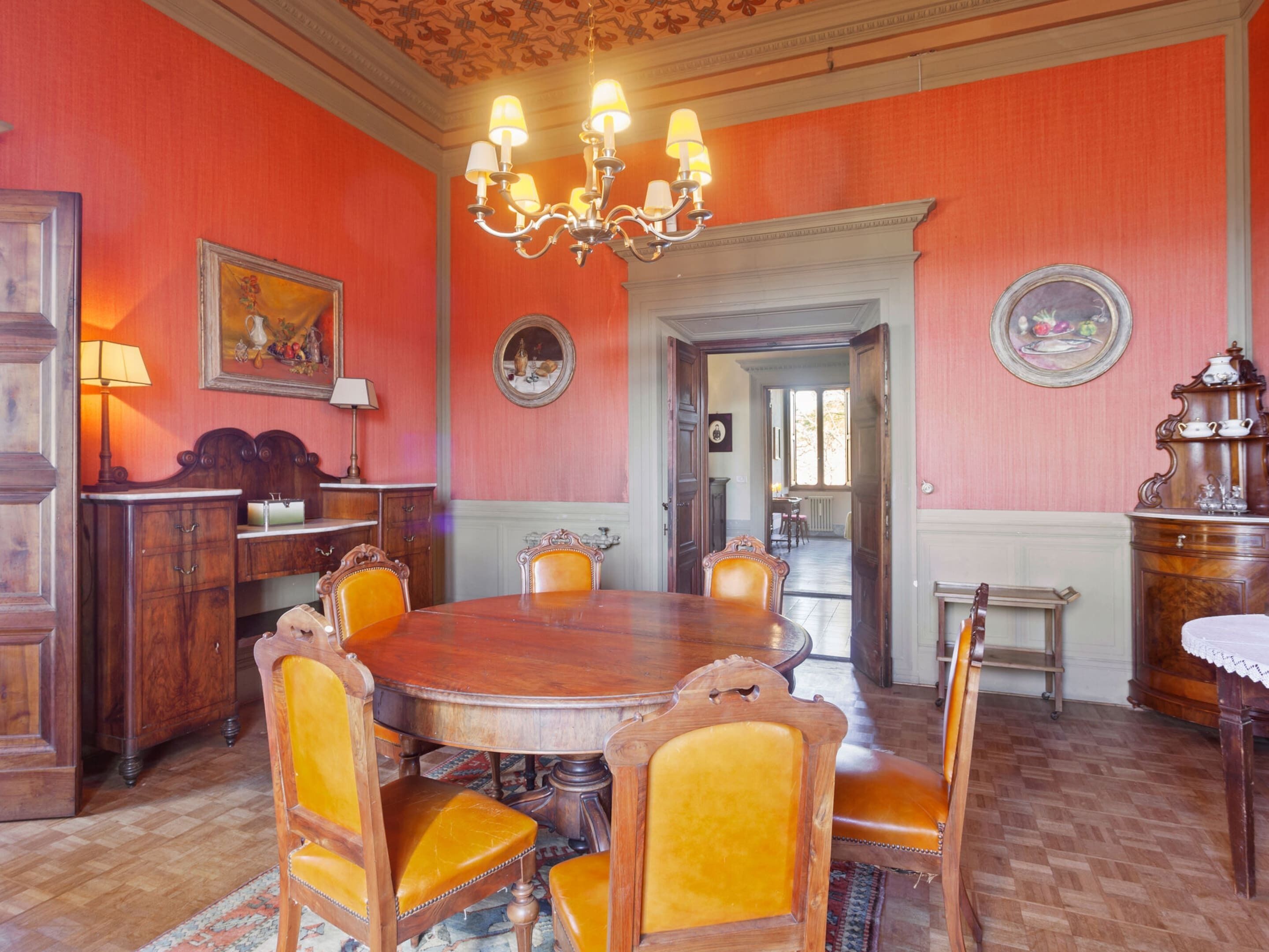 Une salle à manger avec une table et des chaises en bois, un lustre et des murs rouges.