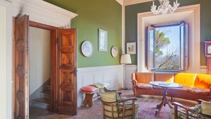 Une pièce avec une porte en bois, un mur vert, une fenêtre donnant sur un paysage, un canapé et une lampe.