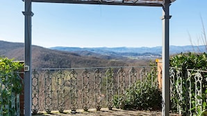 Un espace extérieur abrité, doté d’une rambarde en métal, d  ’un sol en pierre et offrant une vue sur des collines lointaines.