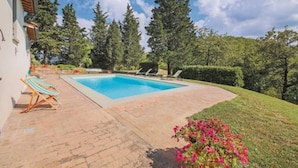 Une piscine entourée de chaises longues, d’une terrasse en briques et de verdure.