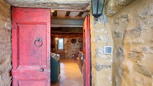 Un intérieur rustique avec des murs en pierre apparentes, une porte rouge et un banc en bois.