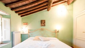 A bedroom with a bed, a radiator, a wooden ceiling, and two wall-mounted lamps.
