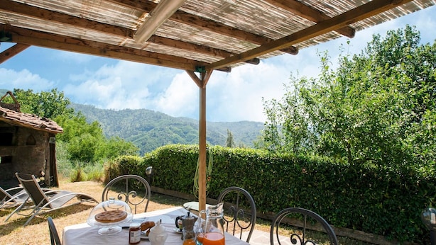 A table set outdoors with breakfast items, a view of a mountain, and a rustic building in the background.