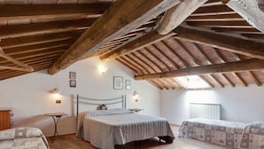 A rustic bedroom with exposed wooden beams, two beds with matching bedding, a small table, and wall-mounted lights. - Holiday Home in Volterra With Pool & Views (Volterra)