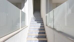 Una escalera con barandilla de vidrio y piso de baldosas, que conduce a un nivel superior.