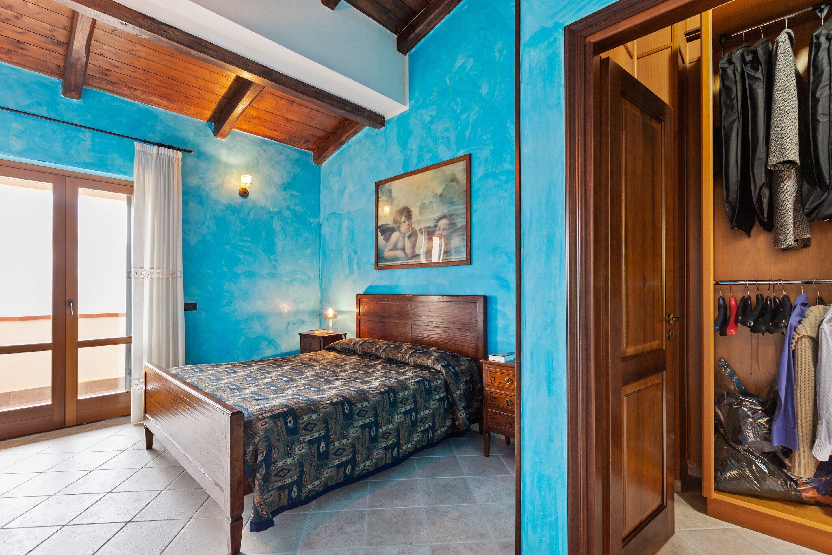 A bedroom with a bed, a nightstand, a wooden wardrobe, and a blue wall.