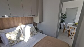 A bedroom with a bed, a wooden headboard, and a small bedside table. There is a doorway leading to a bathroom with a sink and a mirror. - Enticing Mobile Home in Pakoštane With Swimming Pool (Pakostane)