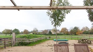 Ein überdachter Außenbereich mit Holzbänken und einem Picknicktisch, mit Blick auf ein eingezäuntes Feld und Häuser im Hintergrund.