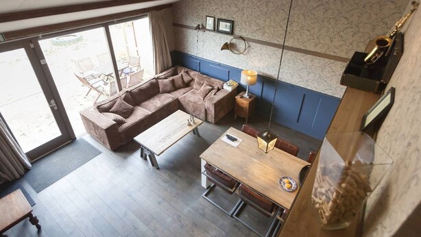 Ein modernes Wohnzimmer mit Sofa, Couchtisch und Esstisch. Ein großes Fenster lässt natürliches Licht herein und bietet einen Blick ins Freie.