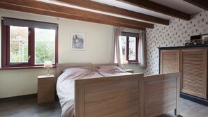 Ein Schlafzimmer mit einem hölzernen Bett, zwei Nachttischen, einem Fenster mit Vorhängen, einem Wandradiator und einem Kleiderschrank.
