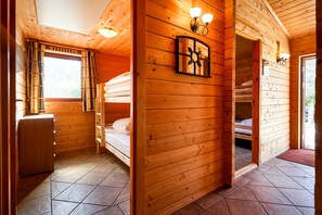 A wooden cabin with a bunk bed, a desk, and a window with curtains.