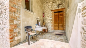 A stone-walled courtyard with a wooden door, a table with a chair, and a fire extinguisher. - Belvilla by OYO Casa Cerbaia Ciliegio (Pennabilli)