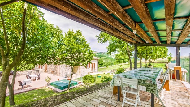 A covered outdoor patio with a table and chairs, a pool, and a stone building in the background. - Belvilla by OYO Casa Cerbaia Ciliegio (Pennabilli)