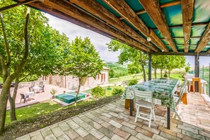 A covered outdoor patio with a table and chairs, a pool, and a stone building in the background.