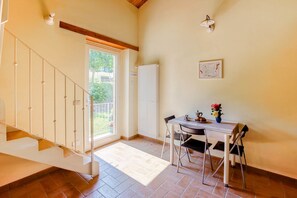 A room with a staircase, a dining table with chairs, a radiator, and a window with a view of greenery.