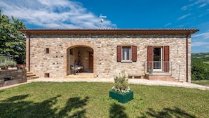 A stone building with an arched entrance, a small porch, and a green planter in the foreground. - Belvilla by OYO Casa Cerbaia Ciliegio (Pennabilli)