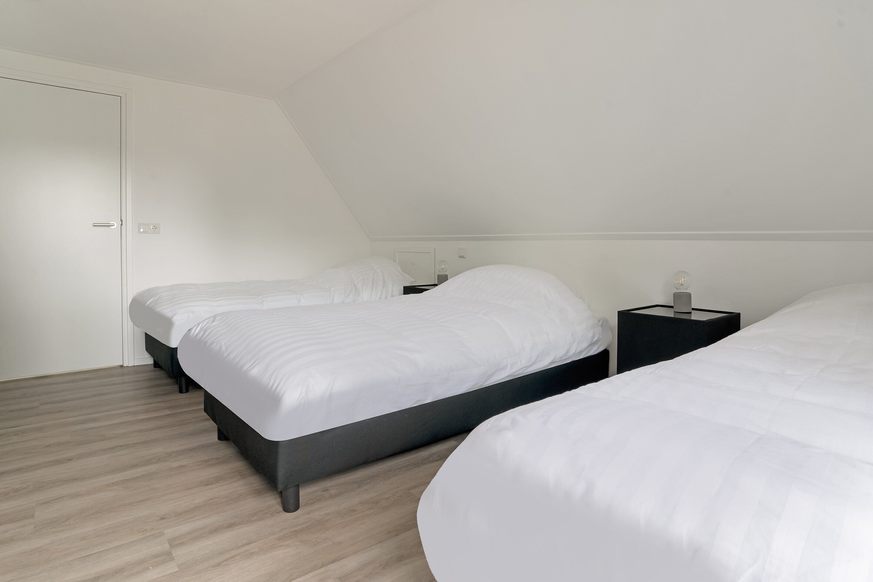 A bedroom with two beds, a wooden floor, and a white door.