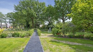 A paved pathway leading through a well-maintained garden with various plants and trees. - Group House in Lemele Near Heuvelrug (Lemele)