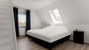 A bedroom with a sloped ceiling, a skylight, a bed with white bedding, a black nightstand, and a radiator. - Group House in Lemele Near Heuvelrug (Lemele)