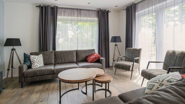 A modern living room with a grey sofa, two round wooden tables, and a grey armchair. - Group House in Lemele Near Heuvelrug (Lemele)