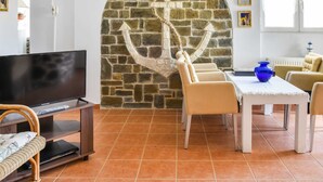 Uma sala de estar com um mural de parede de pedra, televisão, mesa de jantar com cadeiras e uma janela com cortinas.