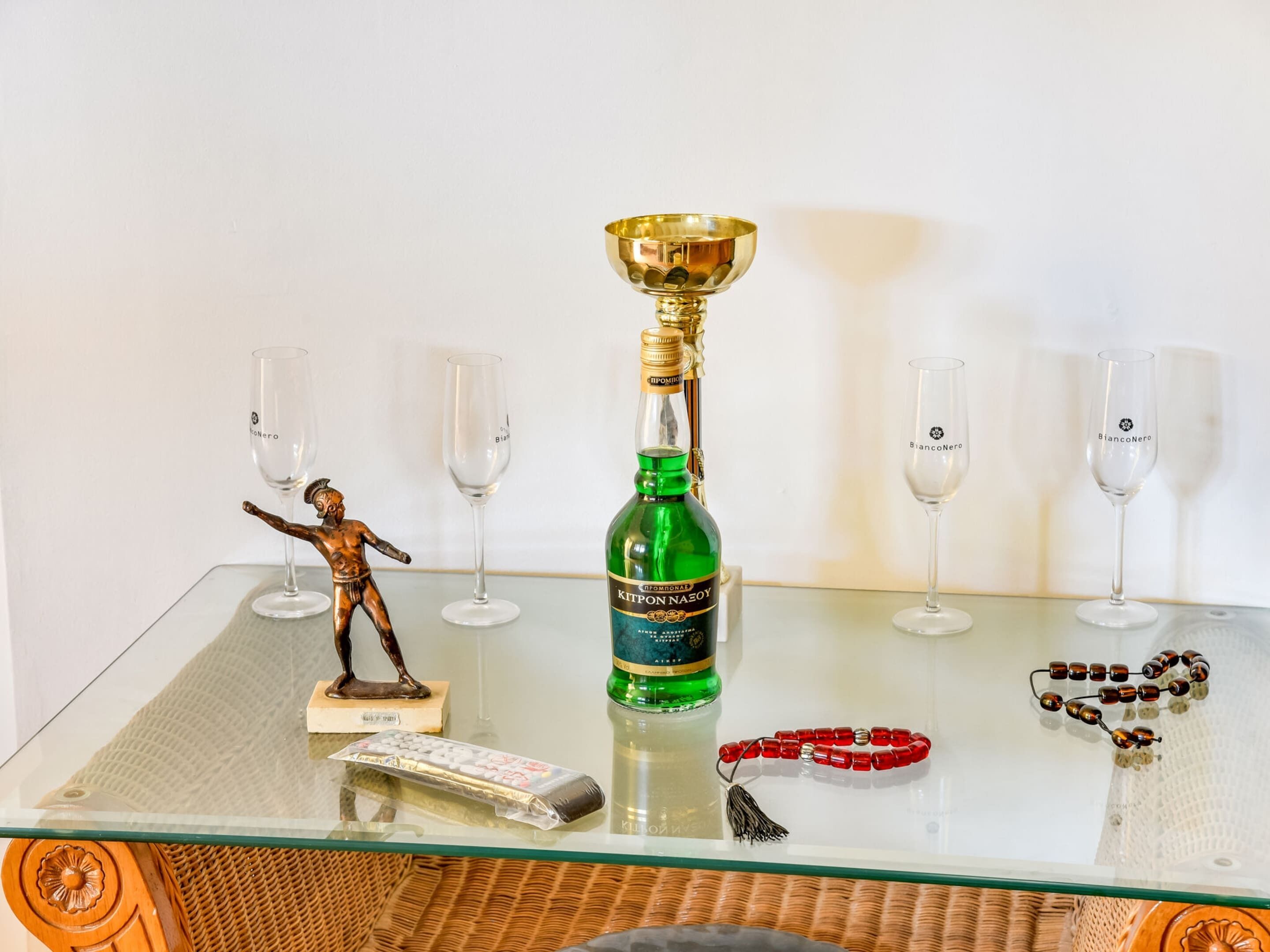 A glass table with a bottle of liquor, a trophy, a remote control, and a rosary.