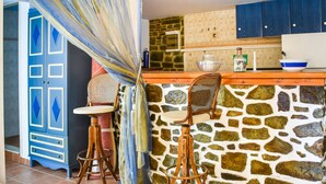 A kitchen with a stone wall, wooden bar stools, a blue cabinet, and a window with curtains. - Alluring Holiday Home in Syros With Barbecue (Syros)