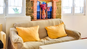 A cozy room with a stone wall, a colorful mural, and a patterned sofa with yellow cushions. - Alluring Holiday Home in Syros With Barbecue (Syros)