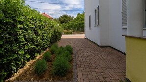 A paved pathway leading to a white building with shutters, surrounded by lush greenery and a clear sky. - Alluring Apartment in Sukošan near Sea (Sukosan)