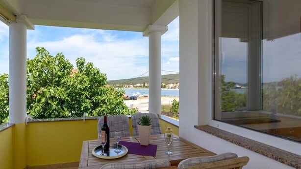 A covered outdoor seating area with a table and chairs, a view of the sea and hills, and a window with a view of the sea. - Alluring Apartment in Sukošan near Sea (Sukosan)