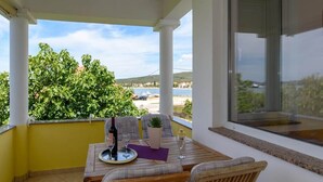 Un área de comedor al aire libre, techada, con una mesa, sillas y vistas al mar y las colinas.