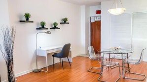 A modern office space with a white desk, a black chair, a glass table with metal chairs, and potted plants on wall-mounted shelves. - Cozy Ocean View Apartment by Miami Te Espera (Hallandale, Miami)