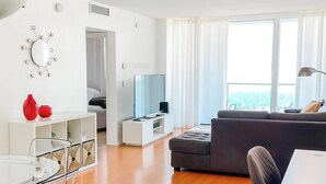 A modern living room with a sofa, a TV, a glass table with chairs, and a white console. - Cozy Ocean View Apartment by Miami Te Espera (Hallandale, Miami)