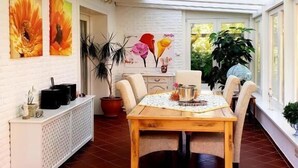 A dining area with a wooden table and chairs, a white buffet unit, and large windows allowing natural light. - White House Ferienwohnung Foehr (Alkersum)