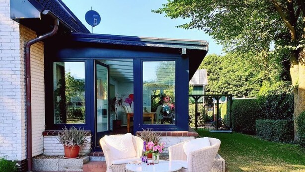 A patio with wicker furniture and a table, surrounded by a brick wall and potted plants. - White House Ferienwohnung Foehr (Alkersum)