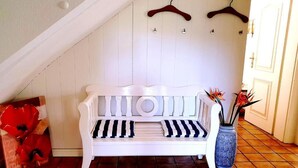 A white bench with black and white striped cushions, a vase with flowers, and wooden hangers on the wall. - White House Ferienwohnung Foehr (Alkersum)
