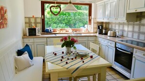 A kitchen with a dining table set for two, a microwave, a kettle, and a stove. - White House Ferienwohnung Foehr (Alkersum)