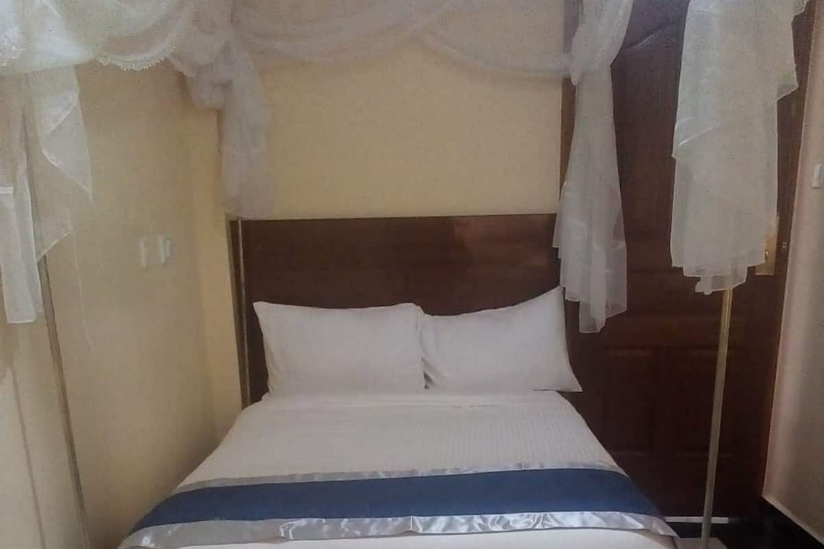 Una cama individual con estructura de madera, ropa de cama blanca y una colcha azul.