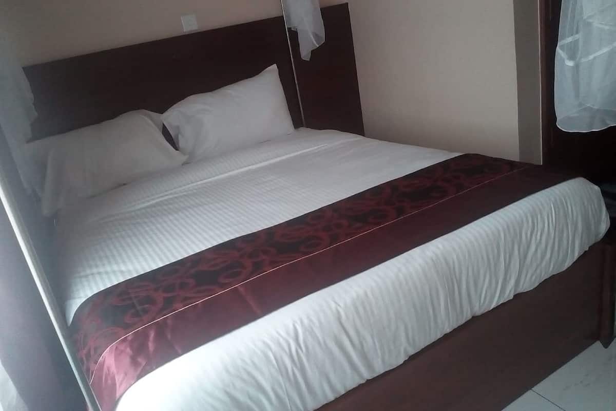 Una cama individual con cabecera de madera, ropa de cama blanca y una colcha estampada roja.