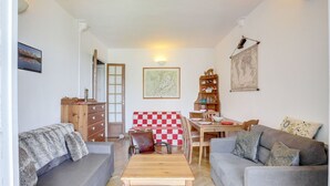 Een gezellige woonkamer met twee grijze banken, een houten salontafel, een eettafel gedekt met borden en glazen, en een boekenkast met decoratieve objecten.