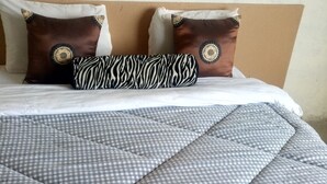 A bed with a checkered duvet cover, two decorative pillows with circular patterns, and a blue towel. - Club 5 Restaurant (Nakuru)