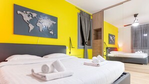 Una habitación de hotel moderna con una cama grande, una cama más pequeña, una obra de arte con un mapa mundial y una pared de color amarillo brillante.