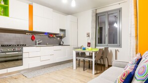 Una cocina moderna con armarios blancos, horno empotrado y comedor con mesa y sillas.