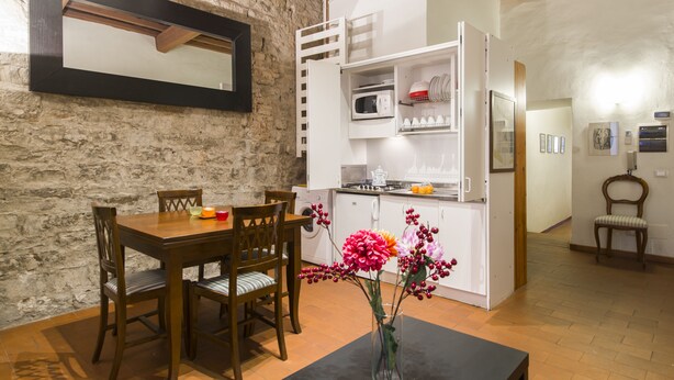 A dining area with a wooden table and chairs, a vase with flowers, and a kitchen area with white cabinets and appliances. - Florence City Center Flat Via Dei Neri (Florence)