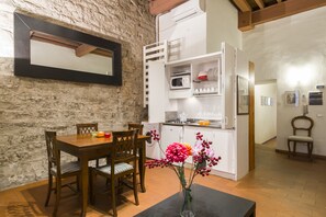 A dining area with a wooden table and chairs, a vase with flowers, and a kitchen area with white cabinets and appliances. - Florence City Center Flat Via Dei Neri (Florence)