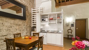 A compact kitchen with white cabinets, a microwave, and a stove. There is a dining table with chairs and a vase of flowers. - Florence City Center Flat Via Dei Neri (Florence)